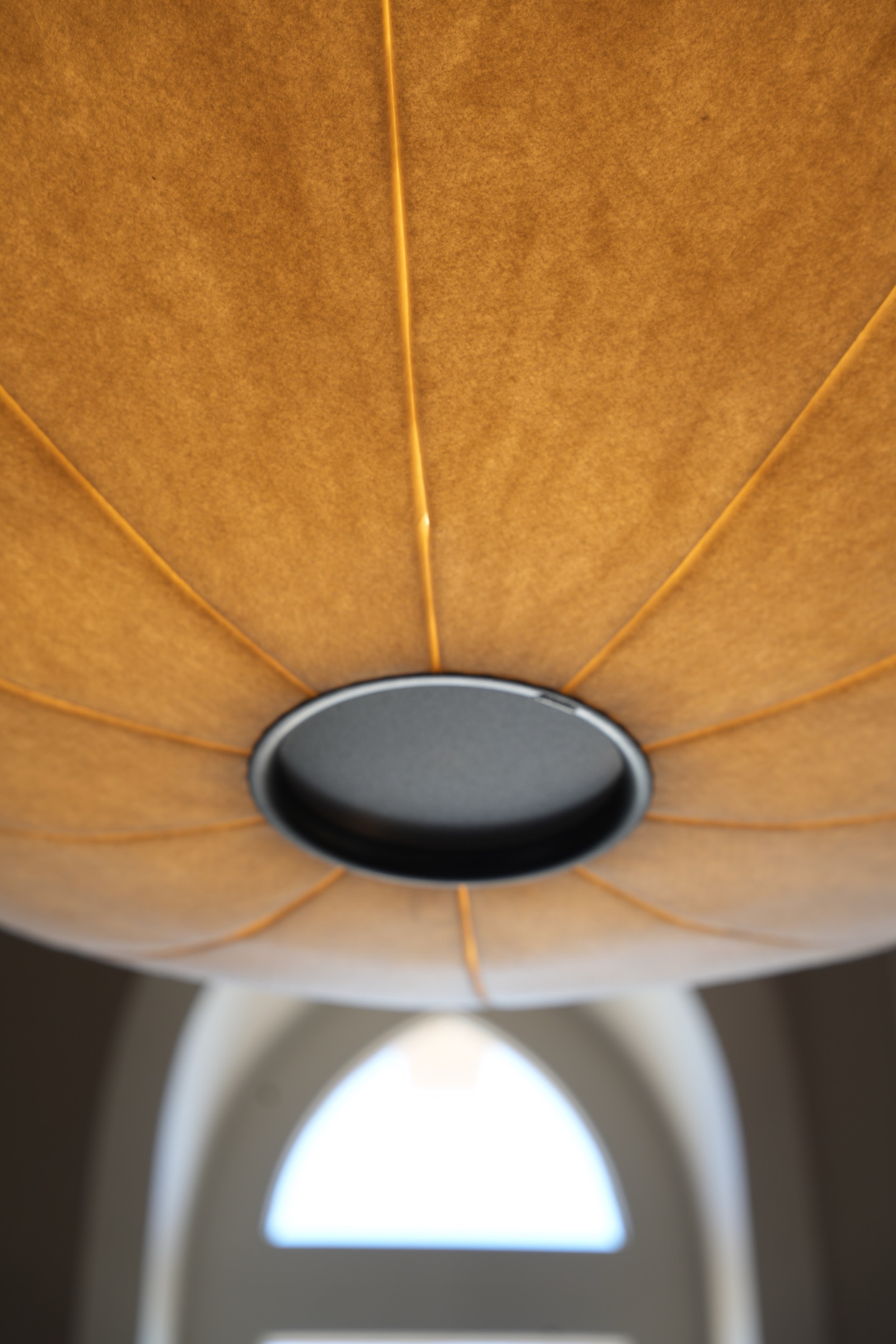 Close view of an amber-lit wool shade and its trim ring above an arched window.