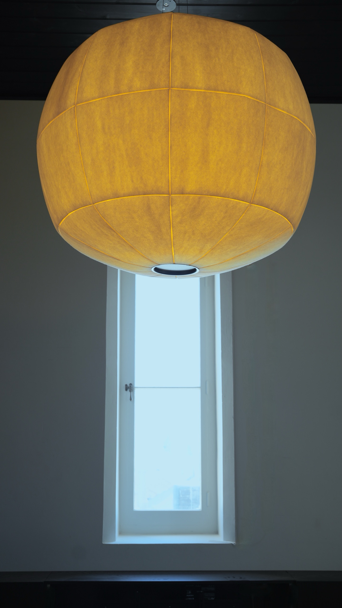 Big Glow pendant lit amber above a tall, narrow timber-framed window in a tower bedroom.
