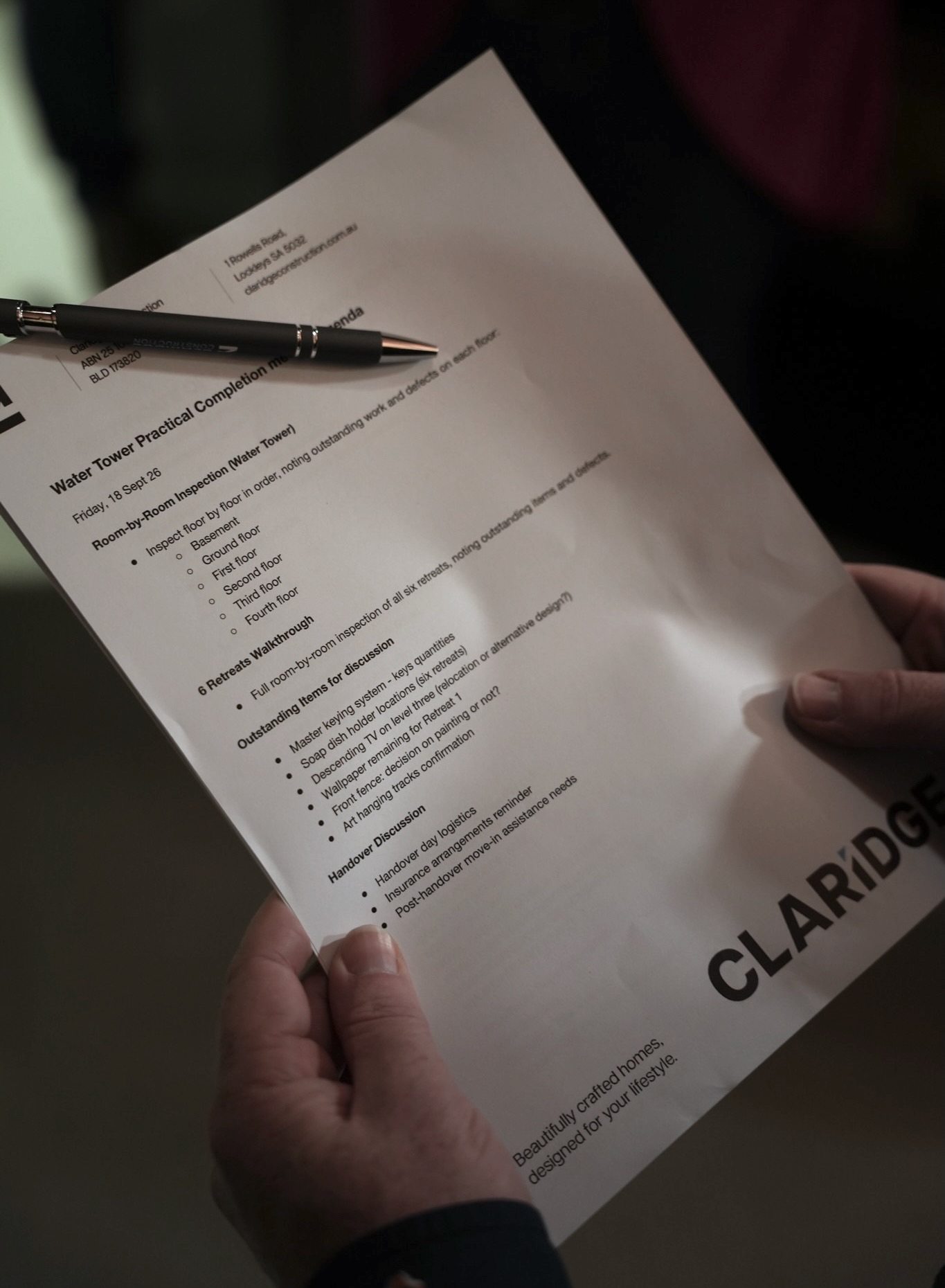Daniel Johnson holds the printed Claridge Construction agenda for the water tower practical completion inspection, a pen clipped to it.
