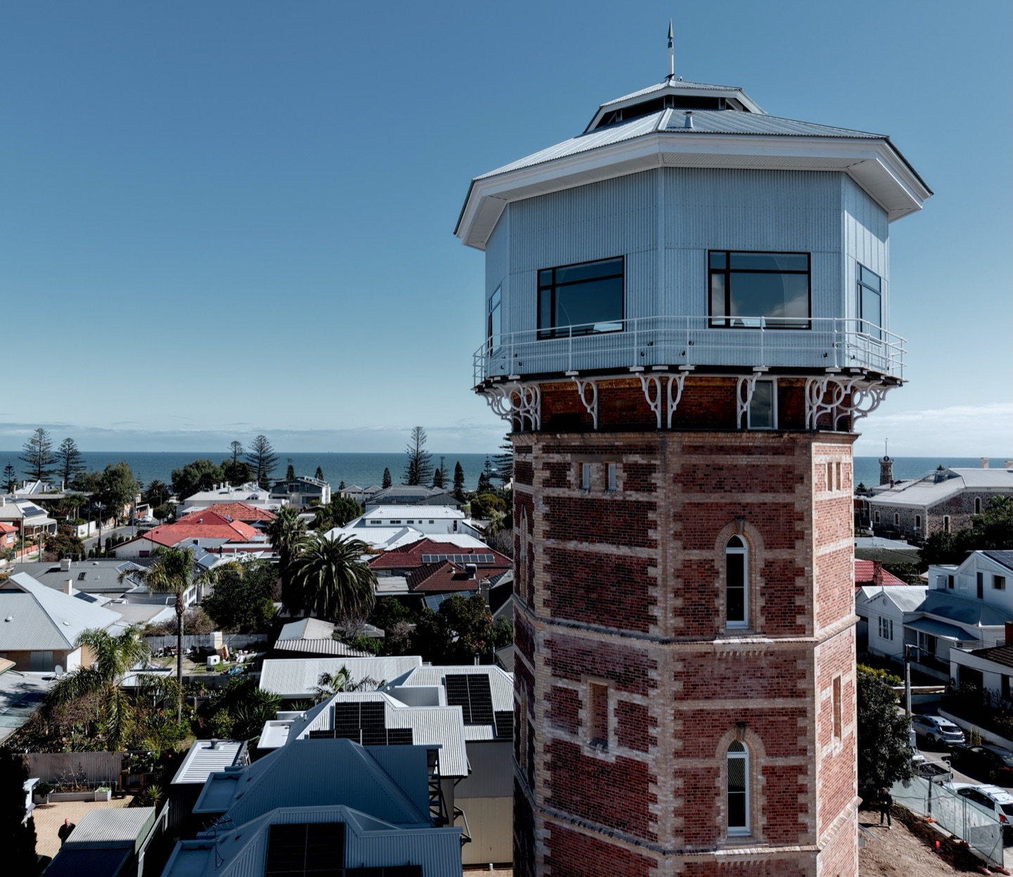 The restored 1880 water tower from the air, its brick shaft topped by the octagonal Observatory, with Semaphore's rooftops and the gulf beyond.